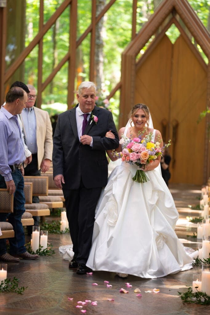 Bride walking down the aisle at Anthony Chapel in Hot Springs, Arkansas, a whimsical wedding venue. Photographed by Maddie, a true to color wedding photographer
