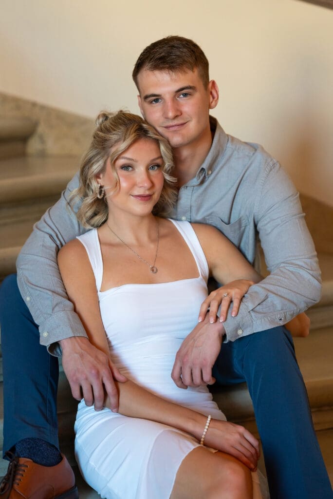 Engagement photo at MN State Capitol shows man and woman seated on steps in calm posed embrace, photographed by Maddie, a true color editorial wedding photographer based out of Baldwin, WI