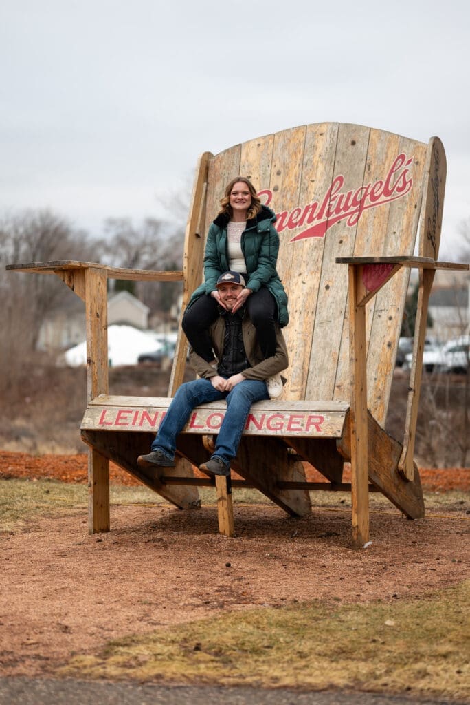 Fun engagement photo in the big chair at Leinenkugel's in Chippewa Falls, WI. True color wedding photographers near Eau Claire