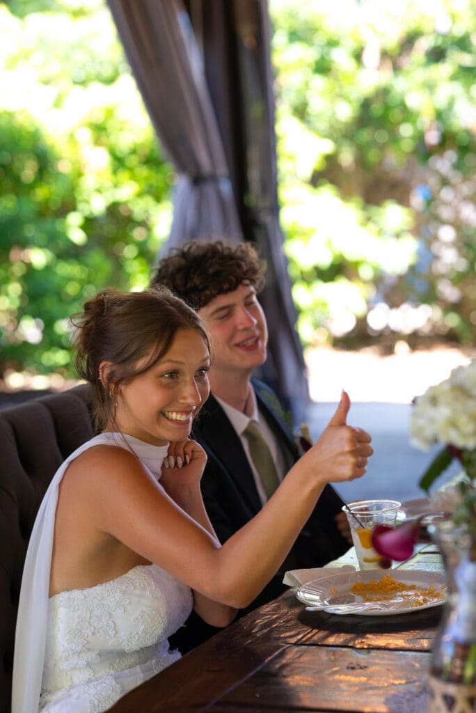 bride gives thumbs up at wedding reception. timeless true to color documentary wedding photographer near me
