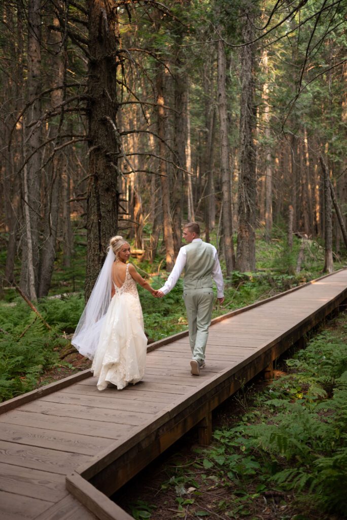 Bride and groom walking along the trail in Glacier NP with the bride looking back at the camera and the groom looking at the bride