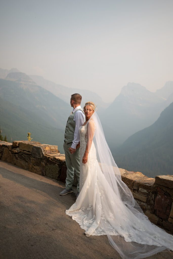 Bride and groom posing very Vogue like at a Glacier National Park overlook with mountains in the background