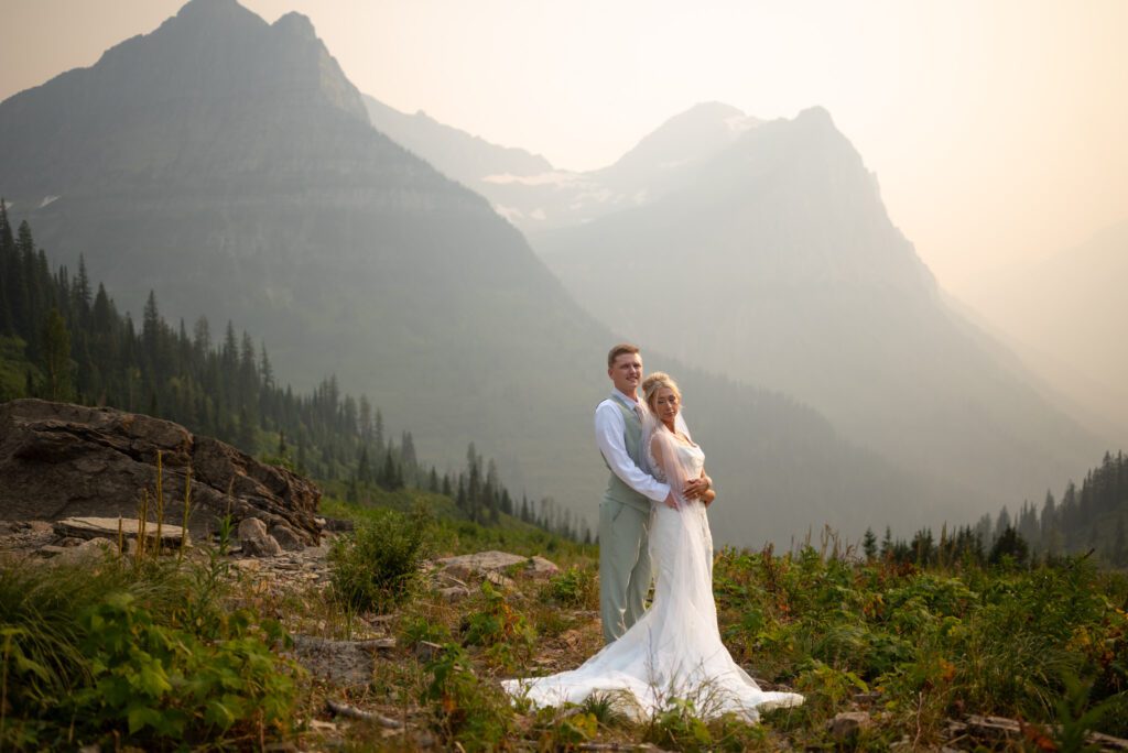 Gorgeous landscape portrait of groom holding bride and mountains in the background with wildfire smoke haze creating dreamy aesthetic