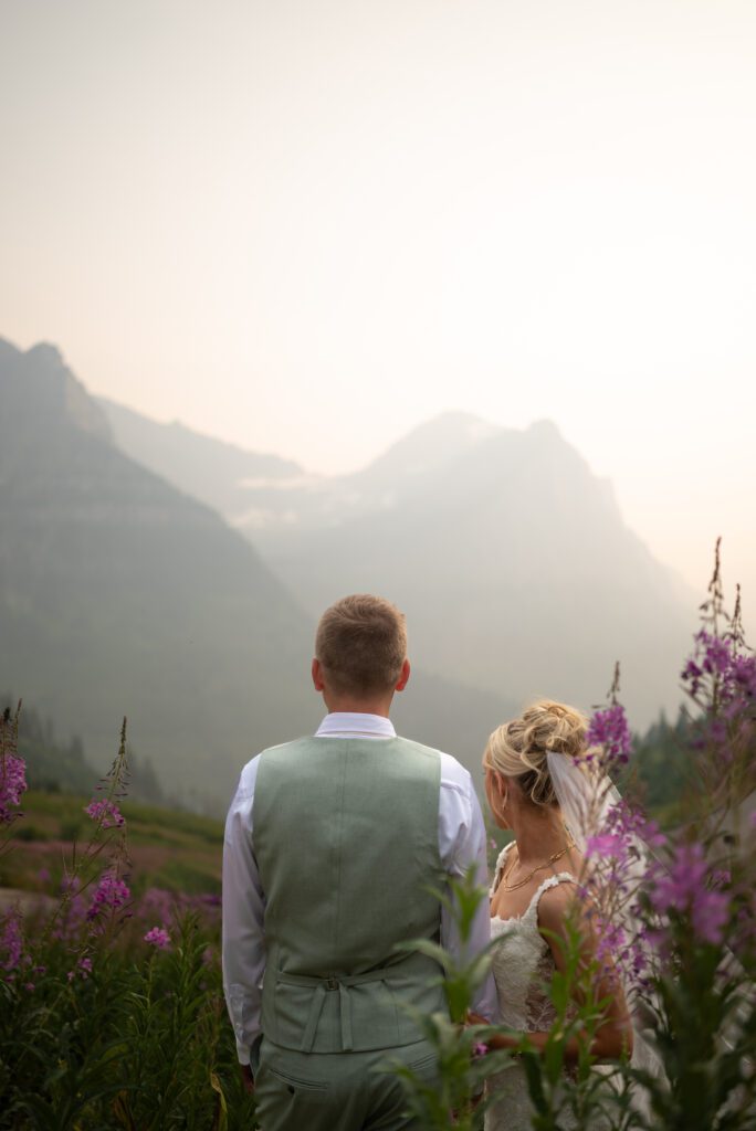 Bride and groom among the purple flowers looking out over the mountains of glacier national park