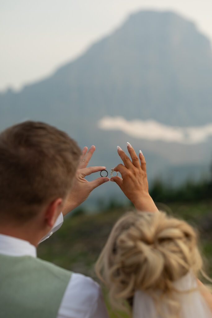 Bride and groom holding rings up with mountains in the background