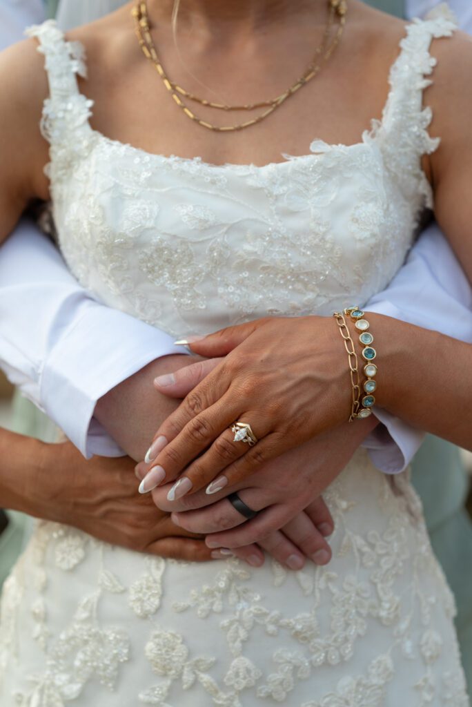 close up image of bride and groom's hands to show rings and jewelry as they hug in an embrace
