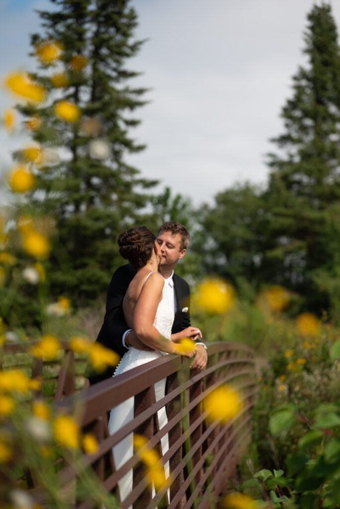 bride and groom kissing on bridge surrounded by yellow flowers