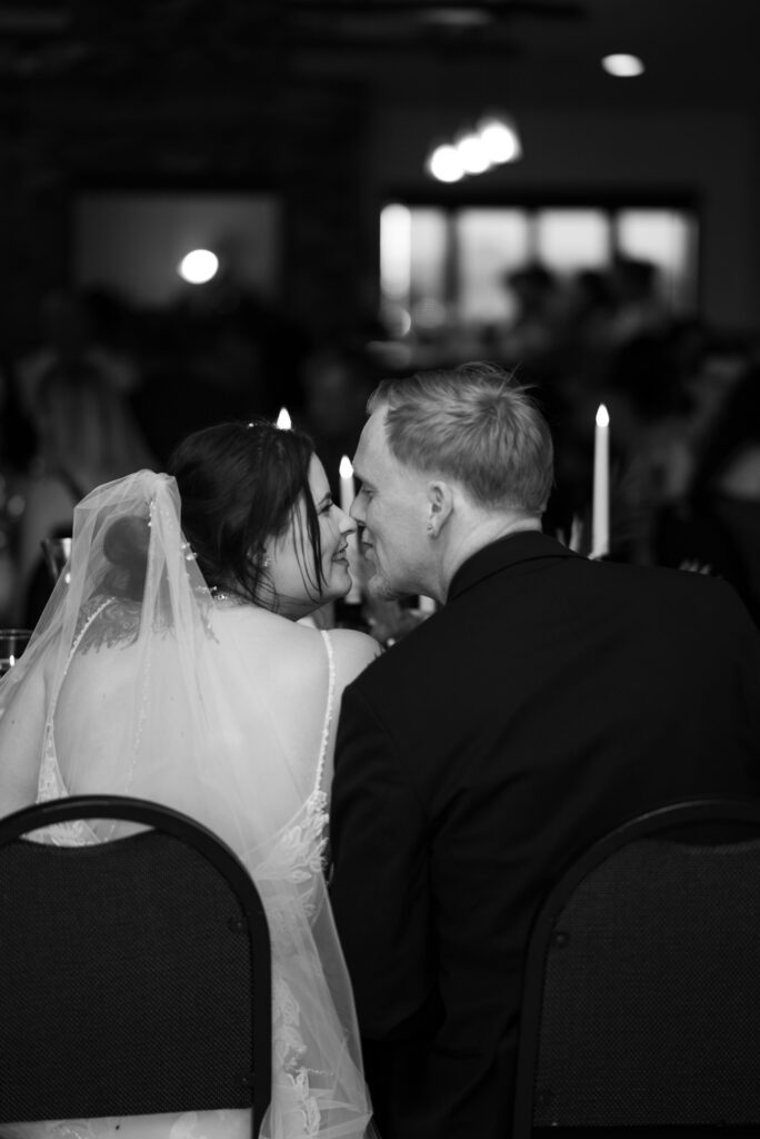 black and white image of bride and groom kissing at head table