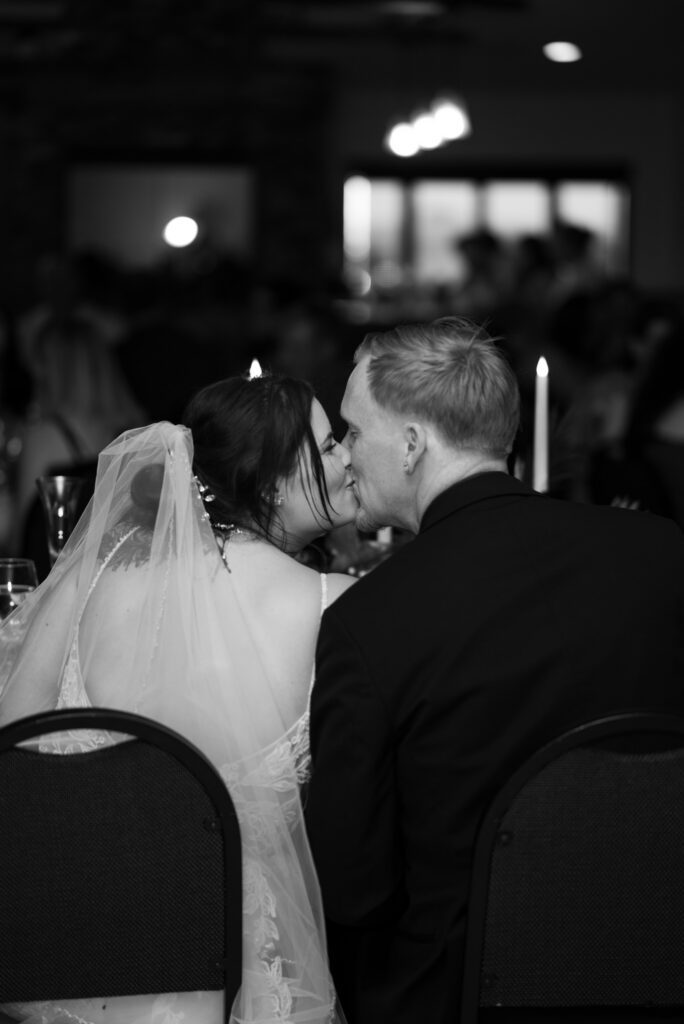 black and white image of bride and groom kissing at head table