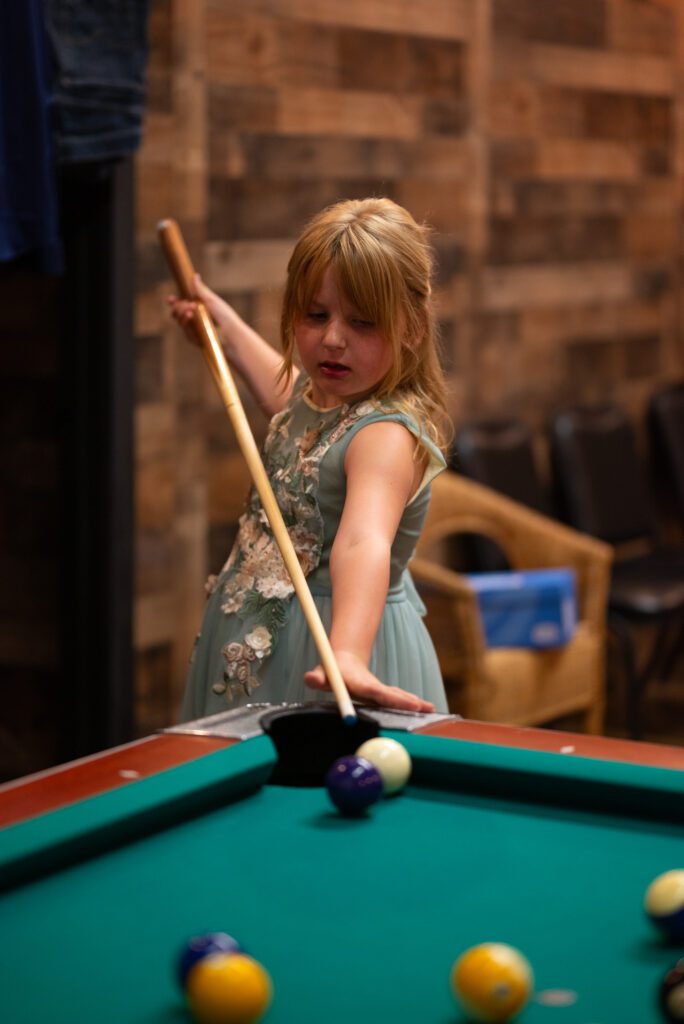 daughter of bride playing pool with mother at Blooming Barrel, a Baldwin wedding venue