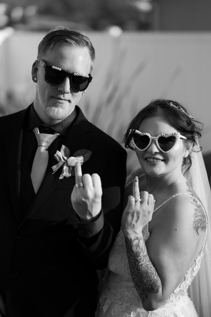black and white image of bride and groom in vintage style wedding sunglasses showing off their ring fingers and rings