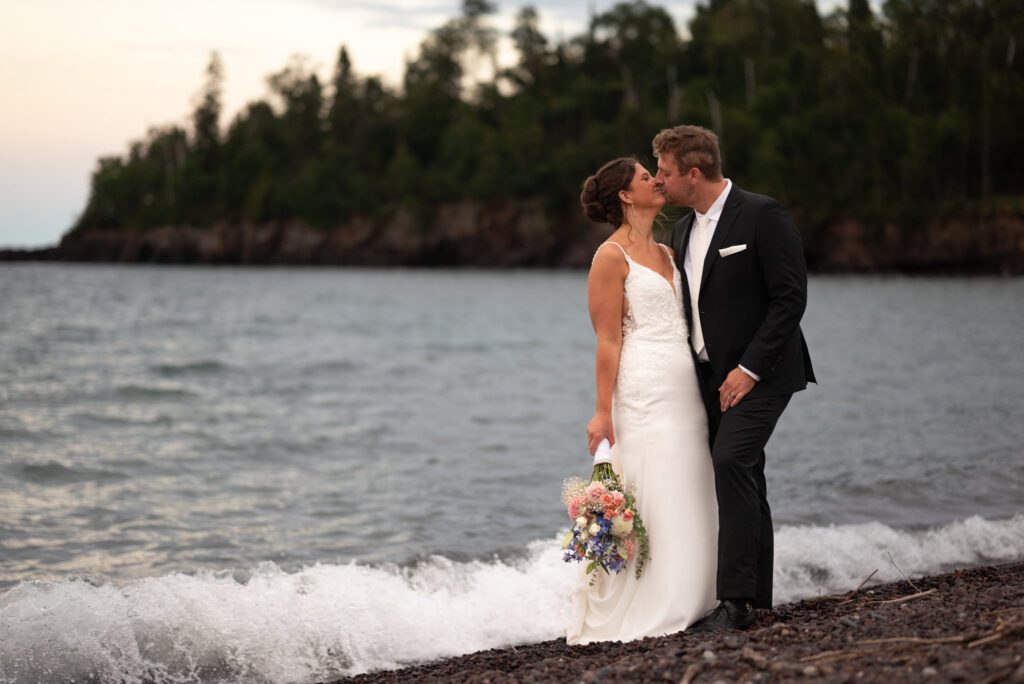 Bride and groom kiss along the shoreline of Lake Superior at Superior Shores Resort in Two Harbors, MN